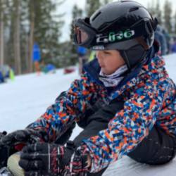 Girl clipping into a snowboard on the mountain with SOS Outreach